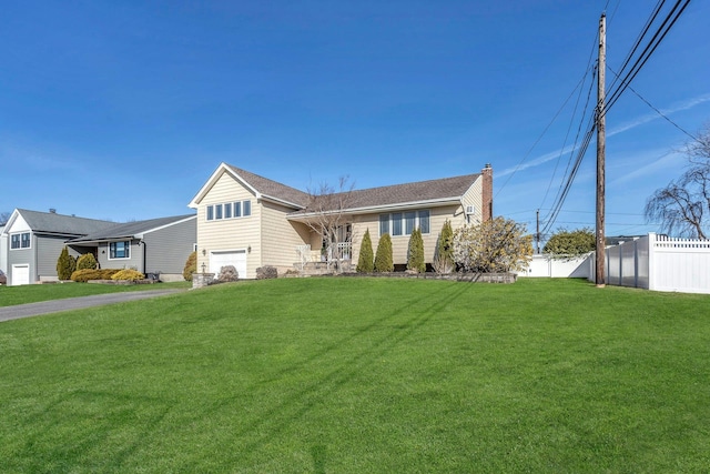 split level home featuring an attached garage, a chimney, a front yard, and fence