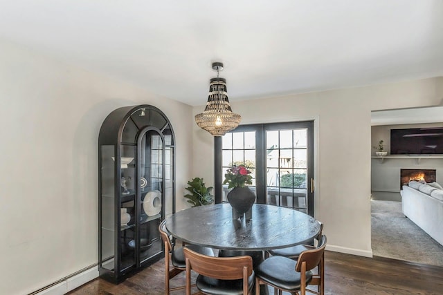 dining room featuring baseboards, baseboard heating, a warm lit fireplace, and dark wood-style flooring