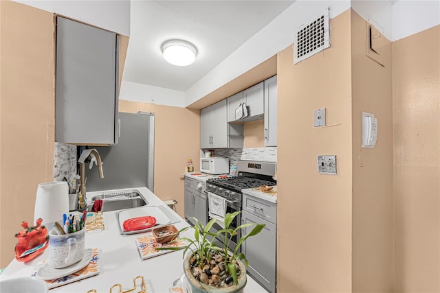 kitchen with tasteful backsplash, gray cabinetry, light countertops, stainless steel appliances, and a sink