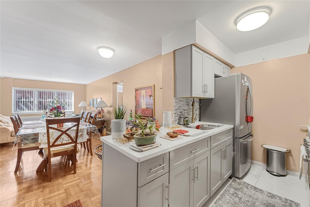 kitchen featuring a sink, gray cabinetry, light countertops, open floor plan, and backsplash