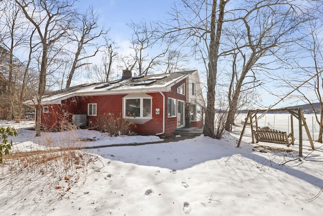 snow covered property with brick siding, central AC, and a chimney