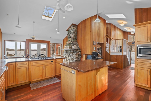 kitchen featuring stainless steel microwave, a breakfast bar area, a skylight, and dark wood-style flooring