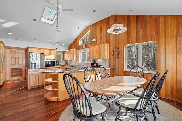 dining space featuring wooden walls, a skylight, dark wood-style floors, high vaulted ceiling, and a ceiling fan