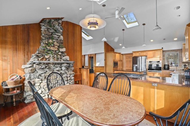 dining room with wood walls, a stone fireplace, a skylight, wood finished floors, and high vaulted ceiling