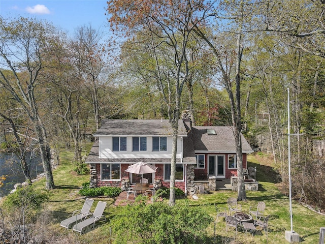 view of front facade with a front lawn, a chimney, a shingled roof, a patio area, and an outdoor fire pit