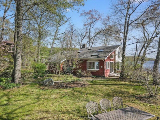 exterior space featuring brick siding, a chimney, a shingled roof, and a front yard