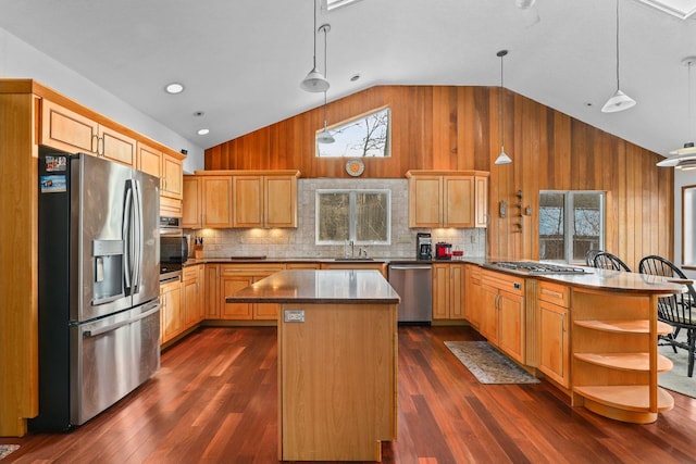 kitchen featuring a peninsula, lofted ceiling, wooden walls, a sink, and stainless steel appliances