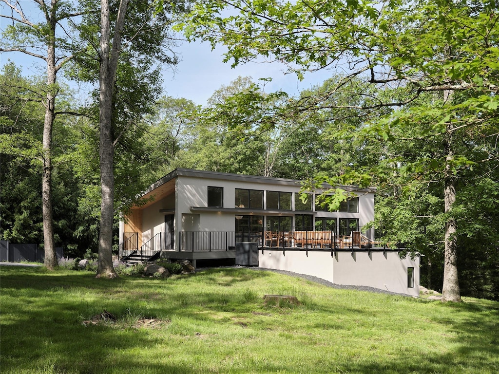 view of front facade with a front yard, stucco siding, central AC, and a wooden deck