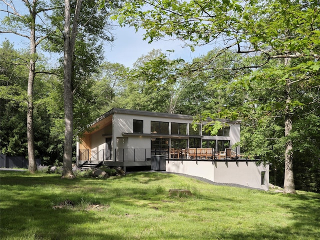 view of front facade with a front yard, stucco siding, central AC, and a wooden deck