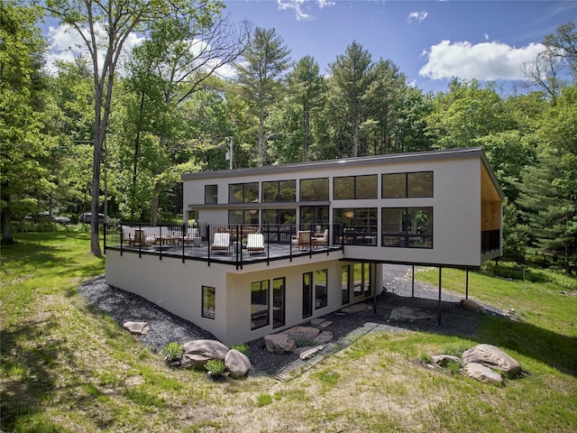 rear view of property featuring a lawn, a wooden deck, and stucco siding