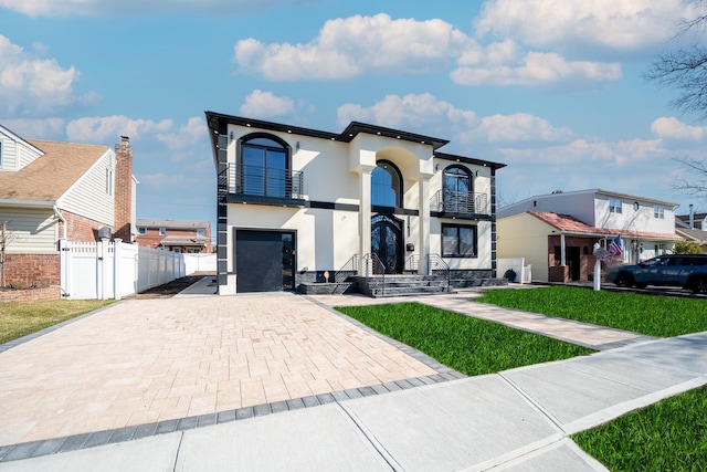 view of front of property featuring stucco siding, decorative driveway, a balcony, and fence