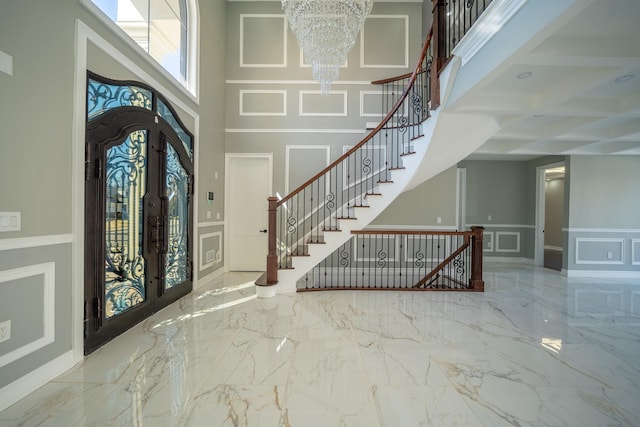 entrance foyer featuring a decorative wall, french doors, a towering ceiling, a notable chandelier, and marble finish floor