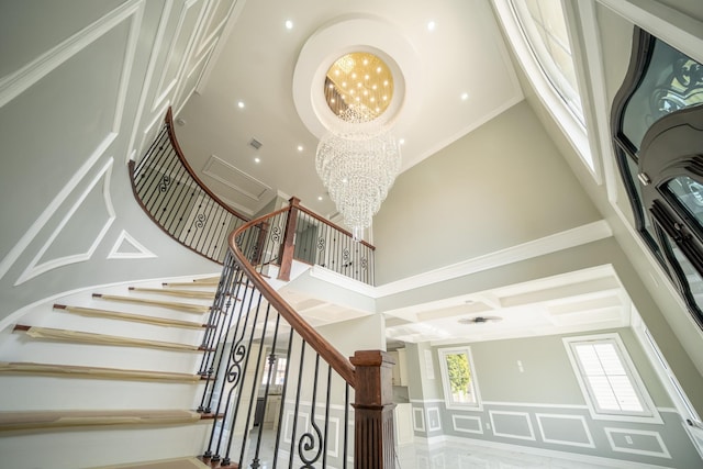 stairs with visible vents, a high ceiling, wainscoting, a decorative wall, and a notable chandelier