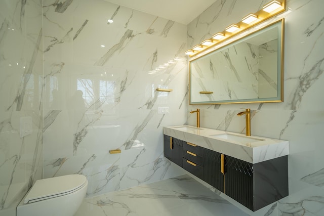 full bathroom with double vanity, marble finish floor, stone wall, and a sink