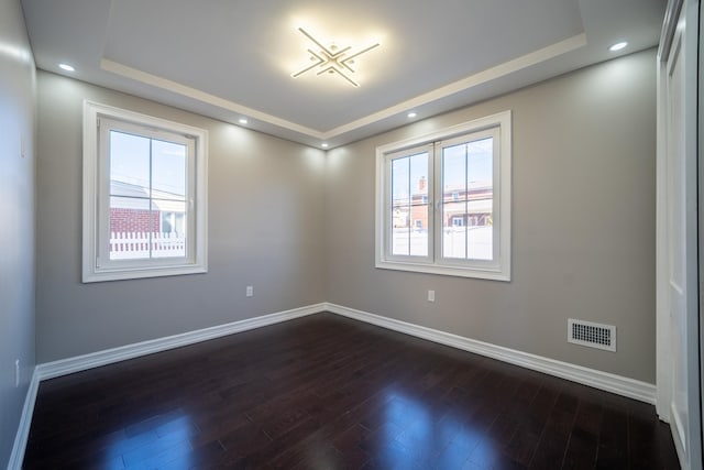 spare room with recessed lighting, baseboards, a raised ceiling, and dark wood-type flooring