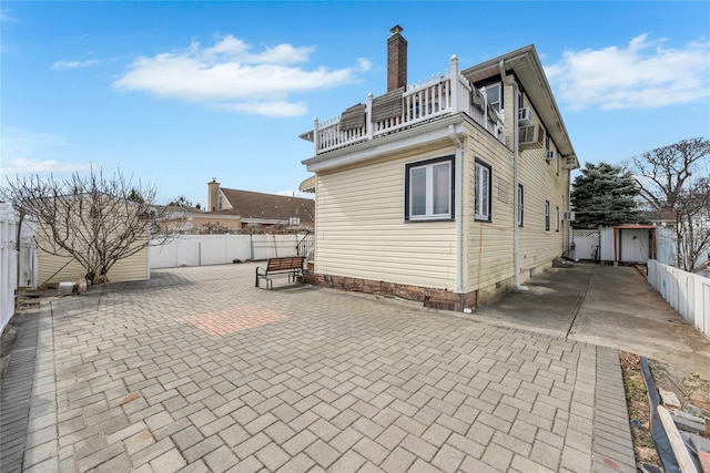 rear view of house featuring a balcony, a patio area, a fenced backyard, and a chimney