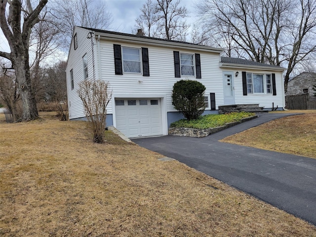 tri-level home featuring a garage, a front lawn, a chimney, and aphalt driveway