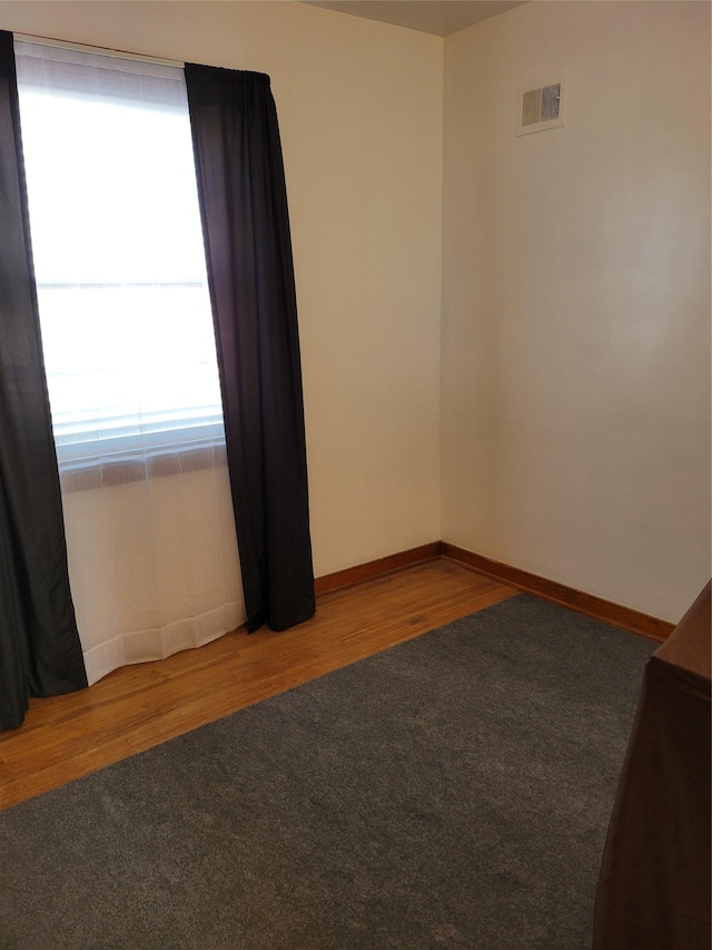 spare room with visible vents, carpet, baseboards, and wood finished floors