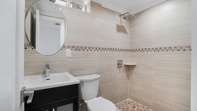 bathroom with a tile shower, toilet, vanity, and tile walls