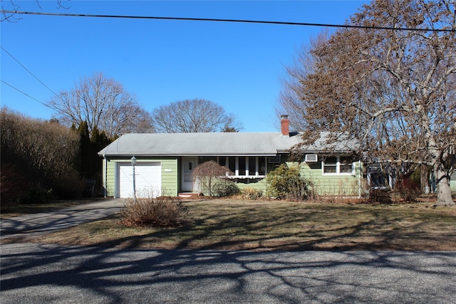 ranch-style home with aphalt driveway, an attached garage, a chimney, and a front yard