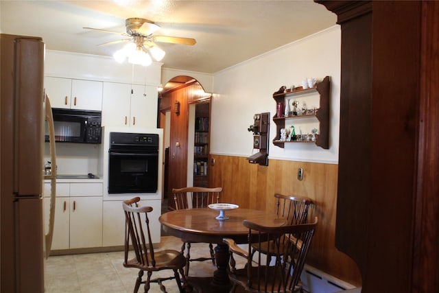 dining room with a ceiling fan, a wainscoted wall, arched walkways, wood walls, and crown molding