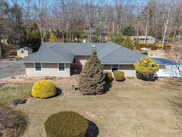 view of front of home featuring driveway, a chimney, a front lawn, and roof with shingles