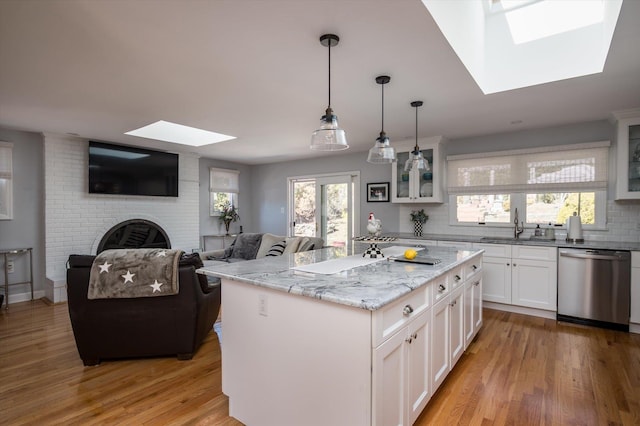 kitchen featuring a sink, stainless steel dishwasher, a skylight, light wood finished floors, and glass insert cabinets