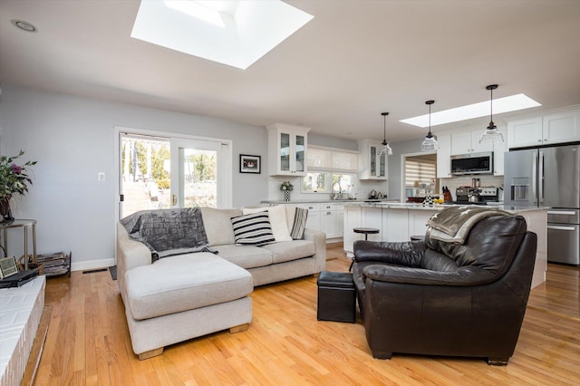 living room with light wood finished floors, visible vents, a skylight, and baseboards