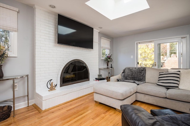 living room featuring wood finished floors, a brick fireplace, a skylight, and a healthy amount of sunlight