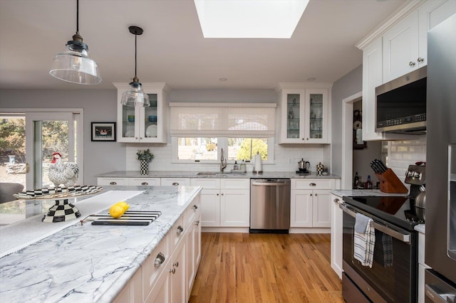 kitchen featuring light stone countertops, light wood finished floors, a sink, stainless steel appliances, and white cabinets