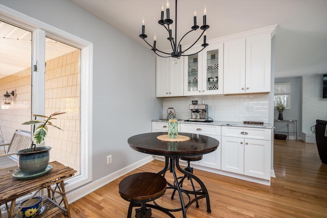 kitchen featuring light wood-type flooring, backsplash, white cabinetry, glass insert cabinets, and baseboards