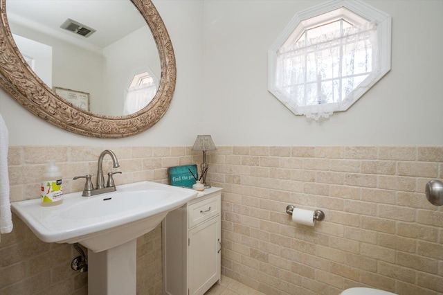 bathroom featuring a sink, visible vents, tile walls, and a wainscoted wall