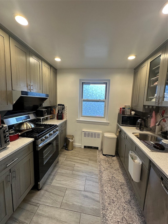 kitchen with radiator heating unit, light countertops, range hood, stainless steel appliances, and a sink