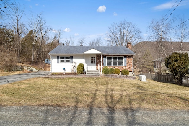 view of front facade with a front yard, fence, a chimney, and a shingled roof