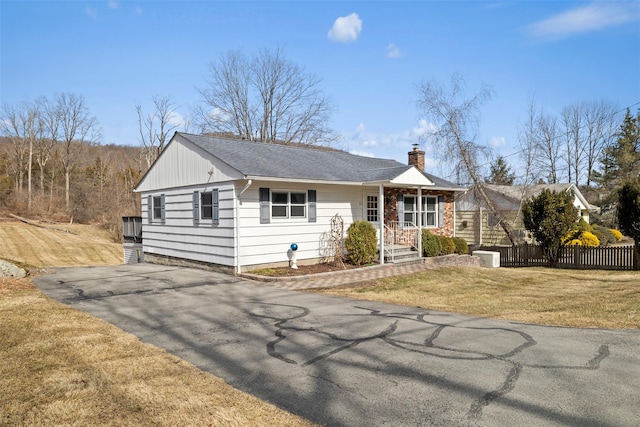 view of front of home with aphalt driveway, a chimney, a front lawn, and fence