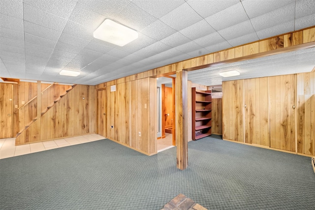 finished below grade area featuring stairway, carpet flooring, and wood walls