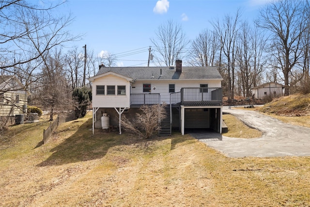 back of property with aphalt driveway, stairway, an attached garage, a wooden deck, and a chimney