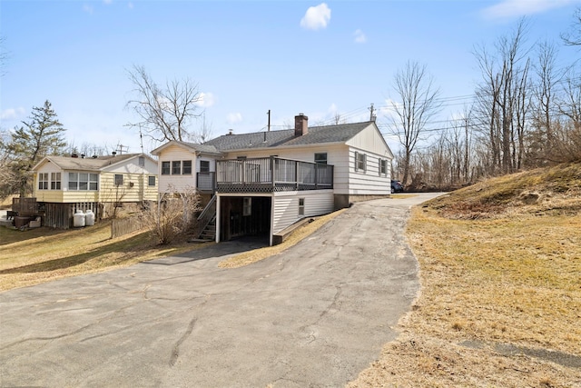 view of front of property with aphalt driveway, a wooden deck, stairs, roof with shingles, and a chimney