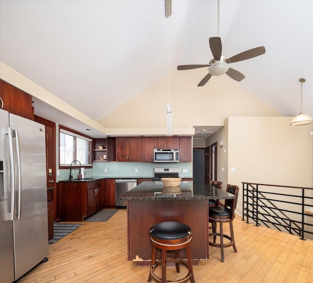 kitchen with light wood-type flooring, a kitchen bar, a sink, a kitchen island, and appliances with stainless steel finishes