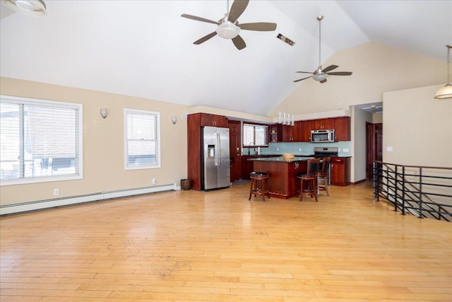 kitchen with dark countertops, a baseboard heating unit, a breakfast bar area, light wood-style flooring, and appliances with stainless steel finishes