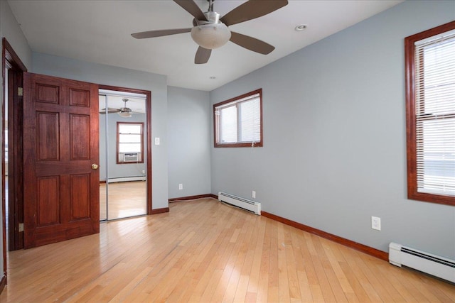 empty room featuring light wood finished floors, baseboard heating, and a healthy amount of sunlight