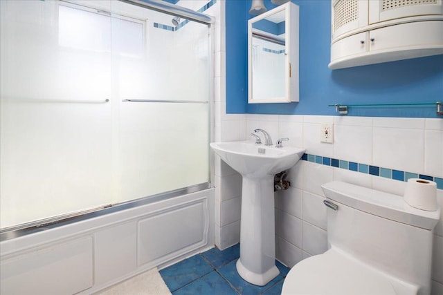 full bathroom featuring toilet, combined bath / shower with glass door, tile walls, wainscoting, and tile patterned flooring