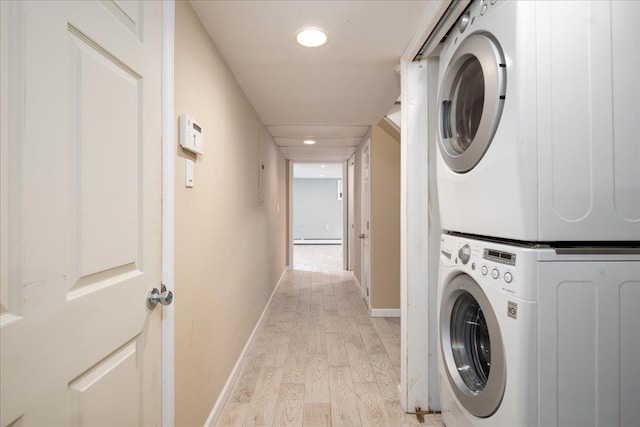 clothes washing area with light wood-style flooring, stacked washing maching and dryer, baseboards, baseboard heating, and laundry area