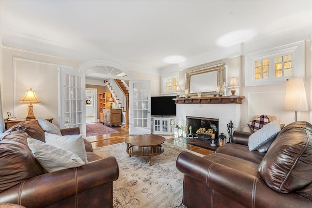 living room featuring wood finished floors, stairway, french doors, crown molding, and a brick fireplace