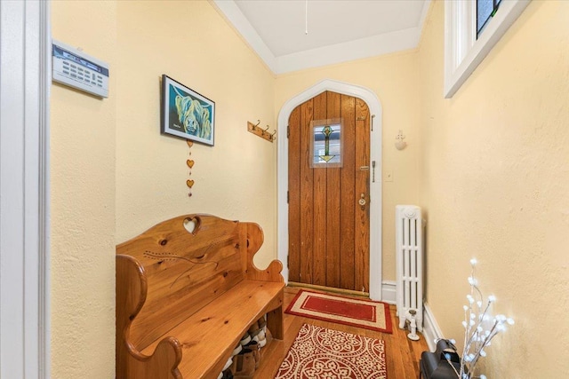 entryway featuring wood finished floors, baseboards, radiator heating unit, arched walkways, and crown molding