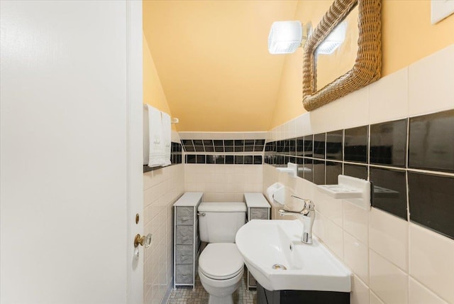 half bath with a sink, lofted ceiling, toilet, and tile walls