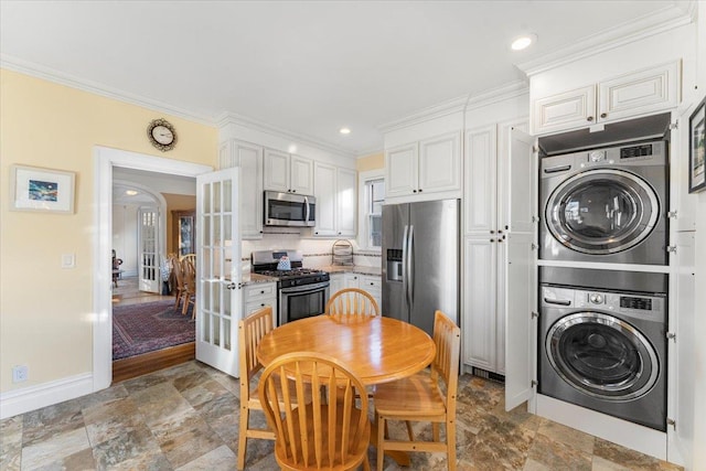 kitchen featuring stone finish flooring, crown molding, appliances with stainless steel finishes, stacked washing maching and dryer, and french doors