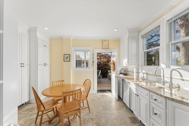 kitchen with ornamental molding, a sink, white cabinets, stone finish floor, and stainless steel dishwasher