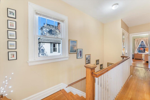 hall featuring an upstairs landing, baseboards, and light wood finished floors