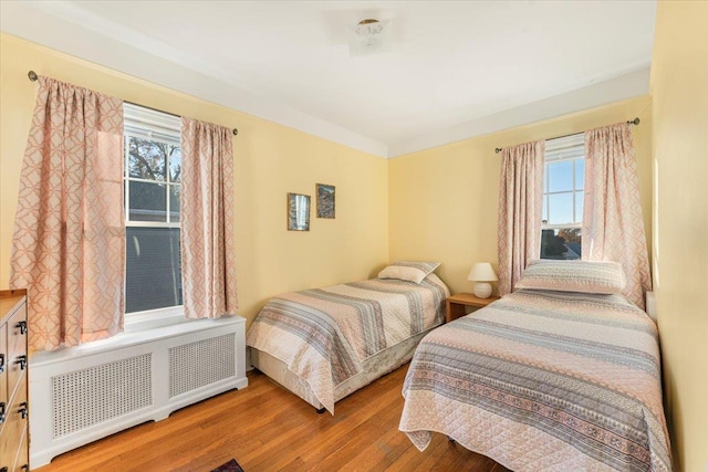 bedroom featuring multiple windows, radiator, and wood finished floors